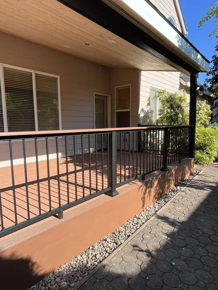 Covered deck with black aluminum railing and a wood-toned top rail running along the side of the house