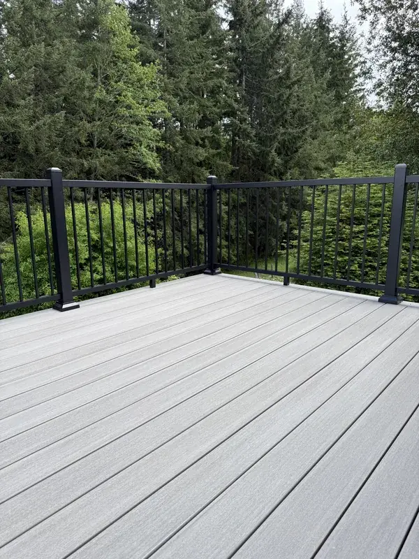The same corner rebuilt in light grey PVC with a black aluminum railing, against the same firs