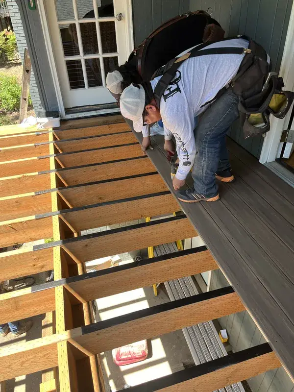 Old surface lifted off, the joists underneath exposed and protected with tape while the crew fastens the first new boards