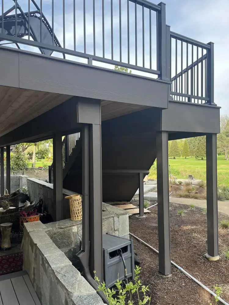 Underside of an elevated deck with wrapped posts and fascia, black aluminum railing above and the fairway beyond