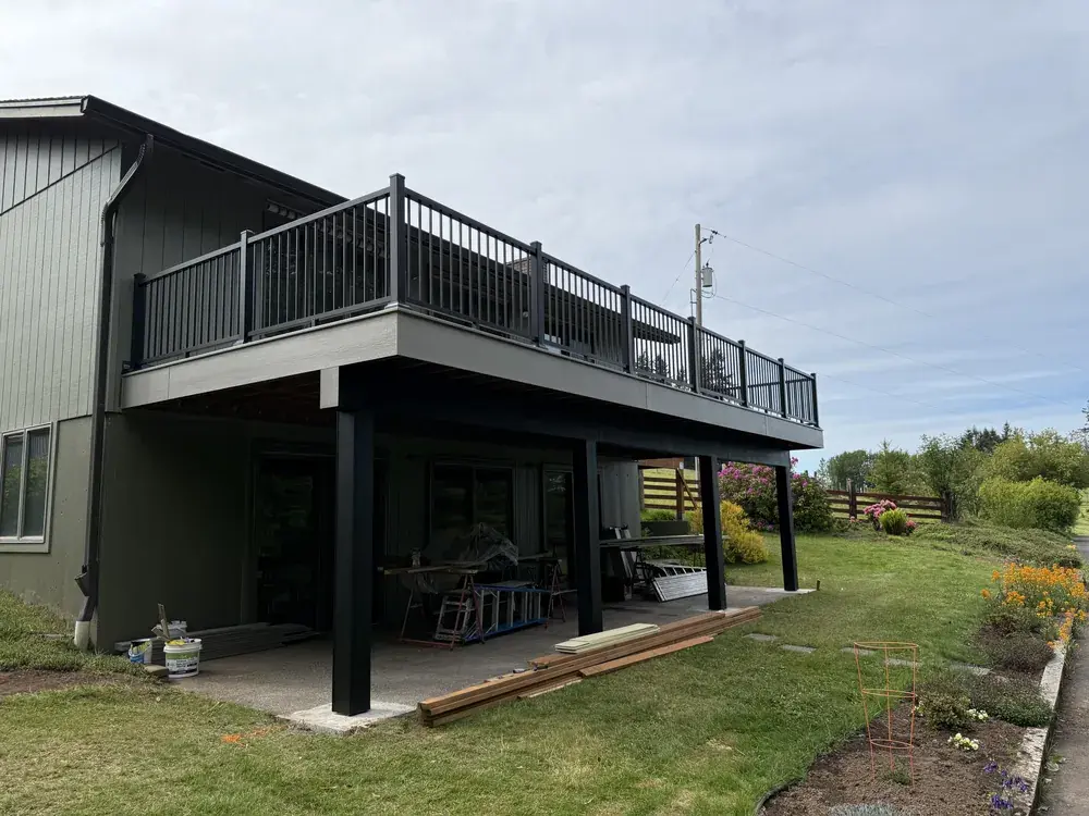 Elevated grey PVC deck with black aluminum railing and wrapped posts along the back of a green home