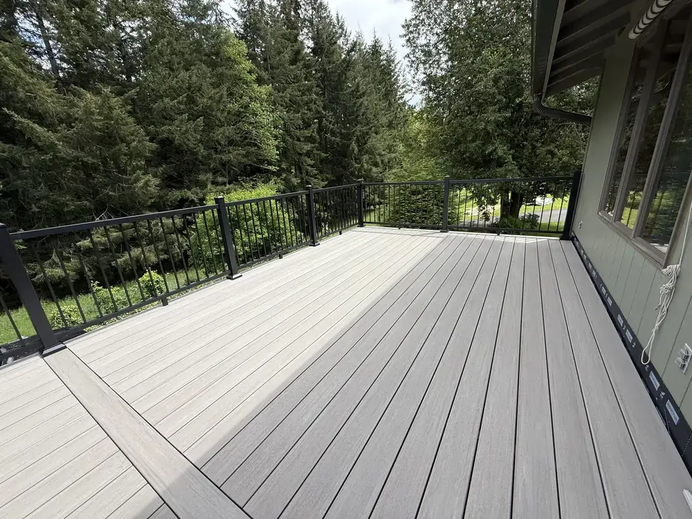 Grey PVC deck with a picture-frame border and black aluminum railing backing onto firs