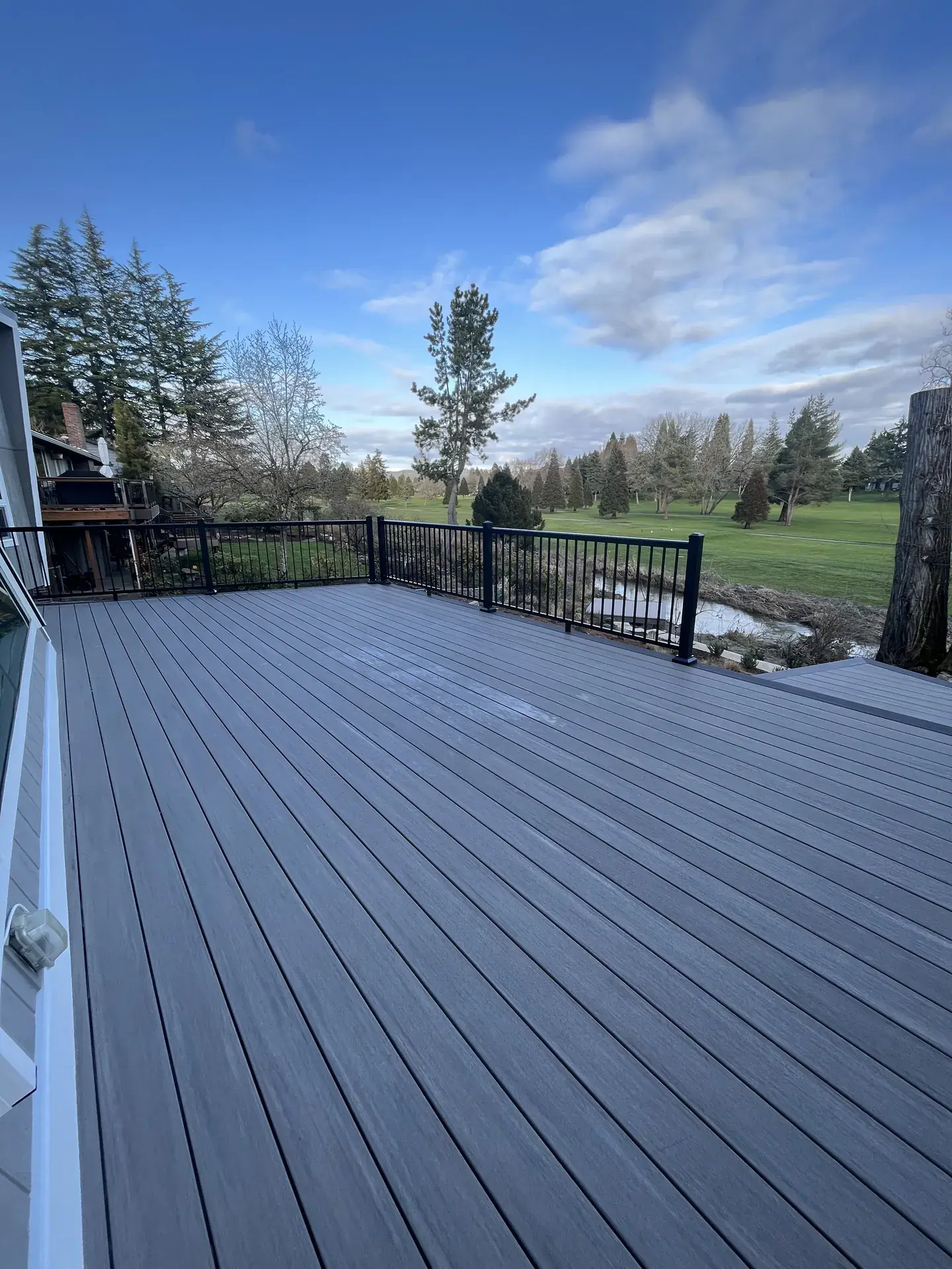 Wide grey PVC deck with black aluminum railing looking out over a creek and the fairways beyond
