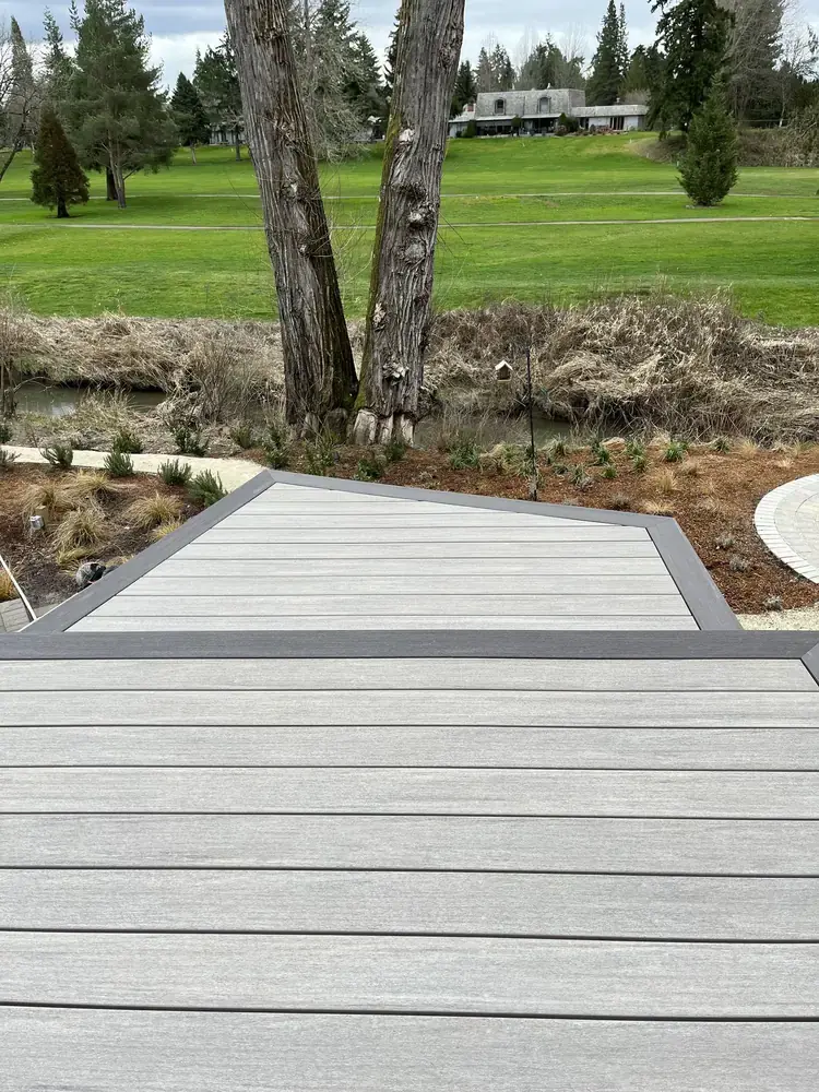 Angled PVC deck landing with a dark border, set above a planted bank with a creek and fairway beyond