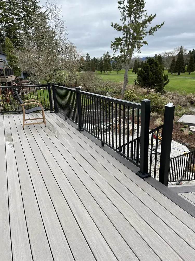 Weathered-grey PVC deck with a single chair and black aluminum railing above a paver patio