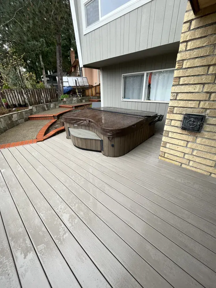 Greige PVC deck laid around an existing hot tub, running up to a brick chimney and a curved brick step