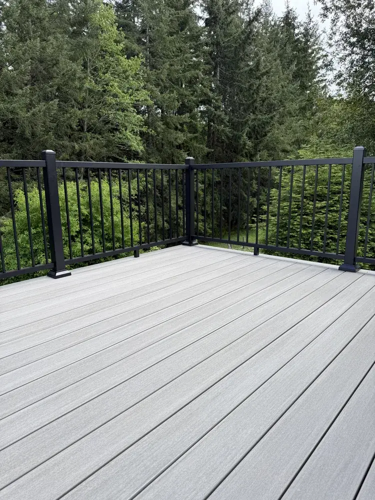 Corner of a pale grey PVC deck with black aluminum railing backing onto Douglas fir