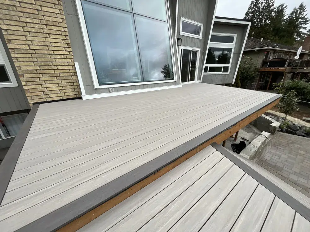 Greige PVC deck with a dark picture-frame border stepping down to a lower level beside a brick and grey-sided home