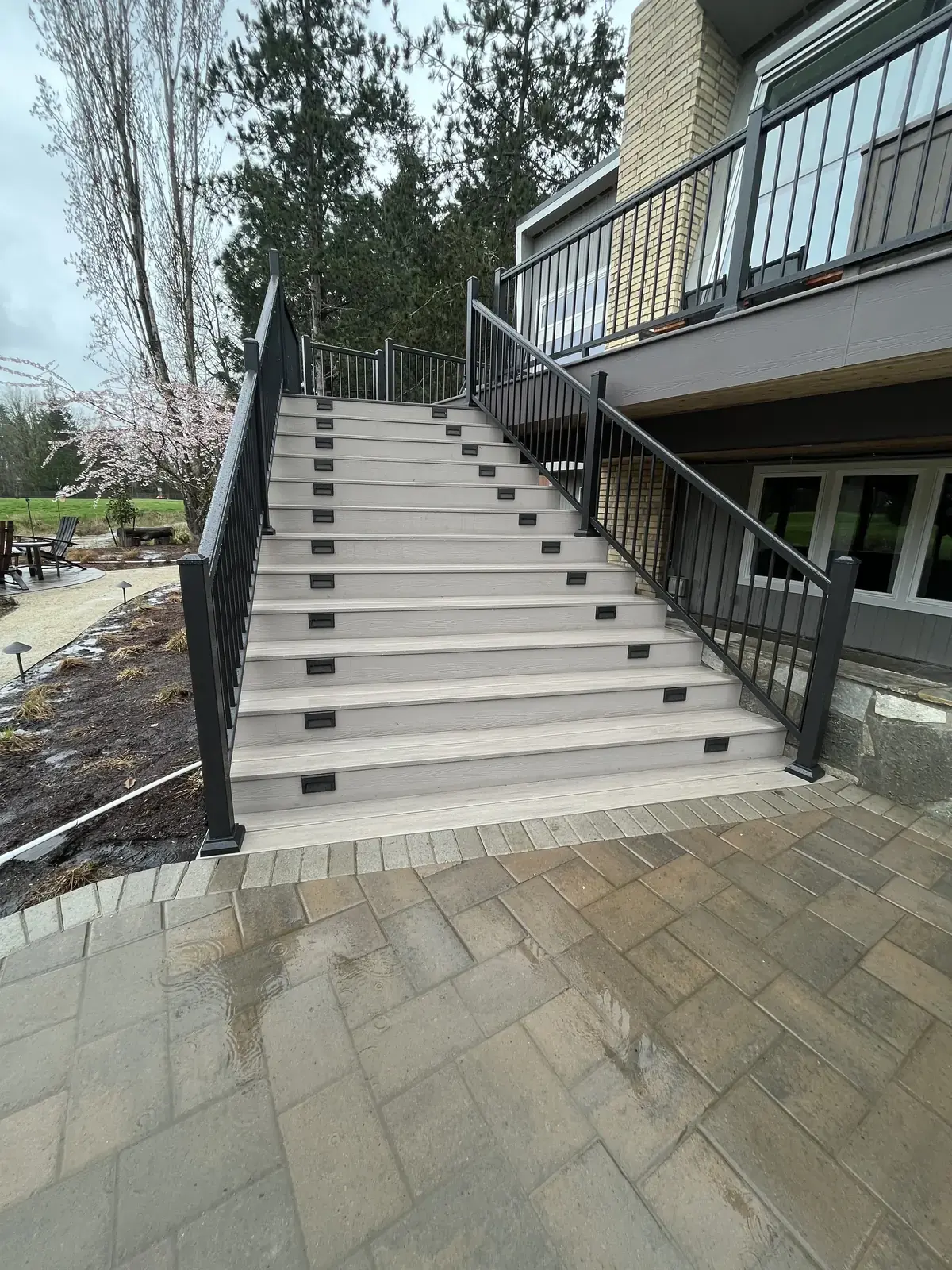 Wide flight of pale PVC stairs with black aluminum railing and lights set into the risers, landing on a paver patio